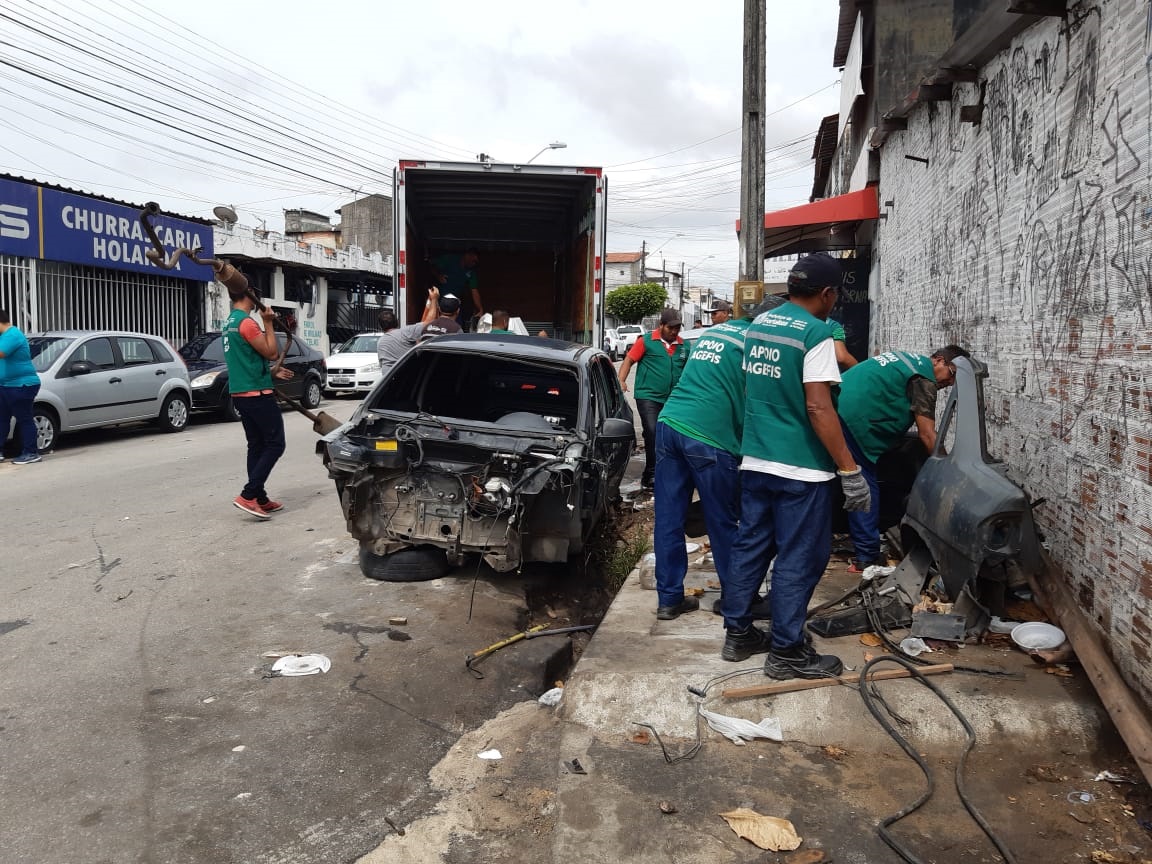 a foto mostra fiscais da prefeitura ao lado da sucata de um carro